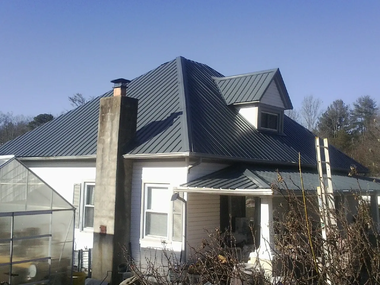 Dark blue standing seam metal roof on a white farmhouse with dormer — Slate & Tile Roof Repair by Roofing Brothers in Laceyville