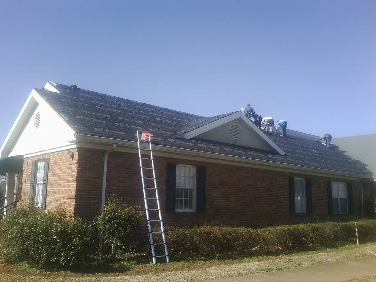 Crew tearing shingles off a brick ranch roof with a ladder set — Emergency Roof Repair work by our crew in Laceyville