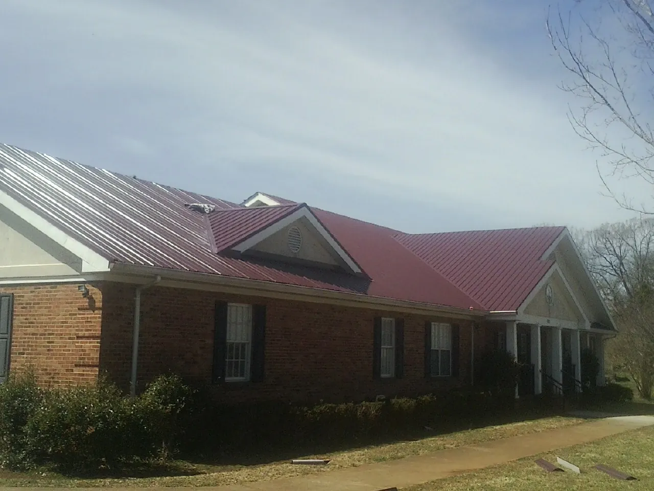 Red metal roof with gabled entries on a long brick building, from a Hail Damage Roof Repair job in Laceyville