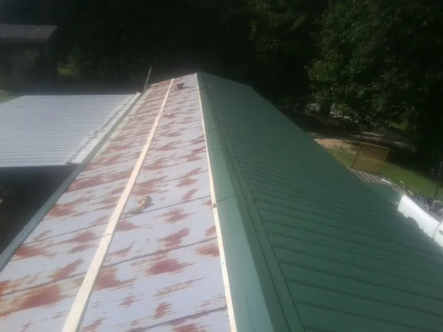 Old rusted panels beside newly installed green metal roofing — Wind Damage Roof Repair by Roofing Brothers in Laceyville