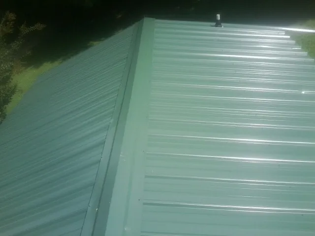 New green metal panels meeting at the ridge of a roof — Flat Roof Repair work by our crew in Laceyville