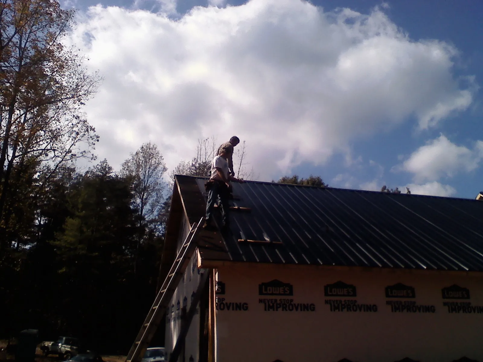 Roofer fastening dark metal panels high against a cloudy sky, from a Roof Inspection job in Laceyville