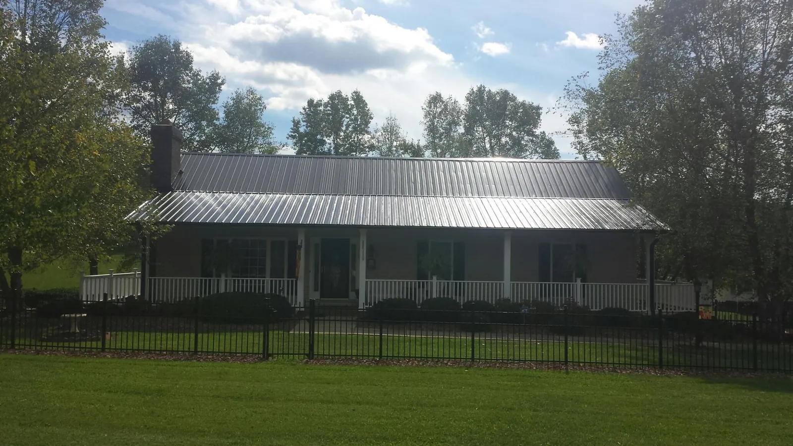 Gray metal roof on a brick ranch with a full width front porch — Gutter Guard Installation work by our crew in Laceyville