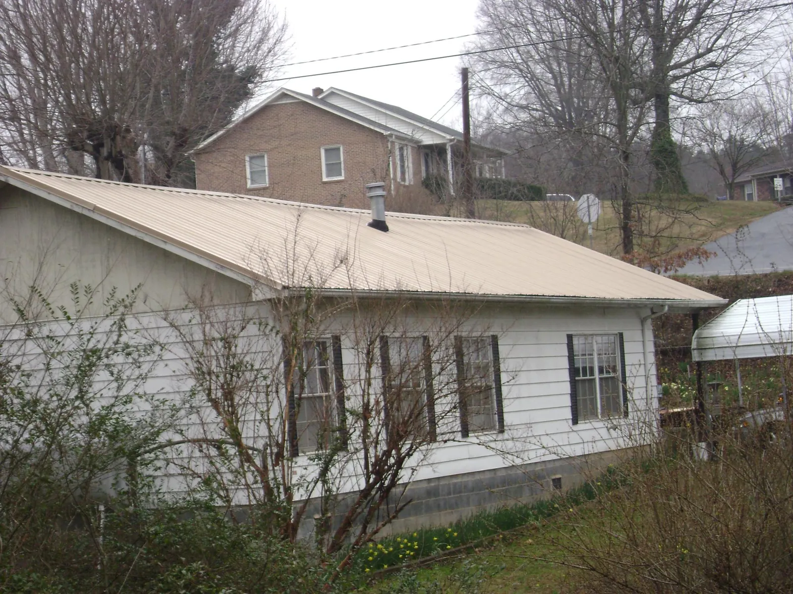 Tan metal roof on a white sided house set into a hillside — Commercial Roofing by Roofing Brothers in Laceyville
