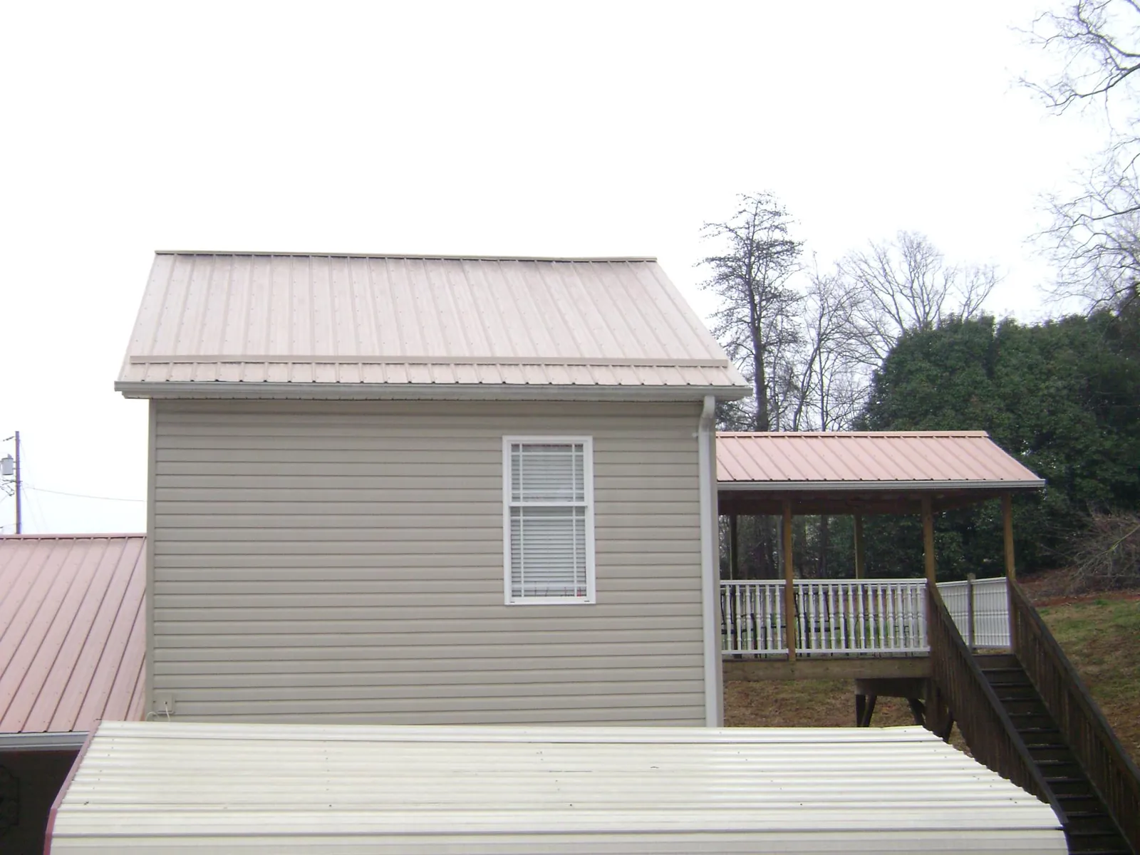 Tan metal roofs on a two story addition and attached porch, from a Roof Replacement job in Laceyville